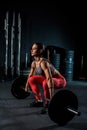 Young, European, muscular girl in red leggings, doing exercise with a barbell in the gym for crossfit. Dark background