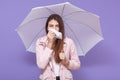 Young European sick young female using paper handkerchief, sneezing, having runny nose, standing under umbrella, feeling unwell,