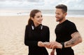 Young european sporty couple working out outdoors at the beach, having break and using mobile phone, standing by seaside