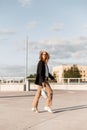 Young European woman model in straw hat in black blazer in fashionable pants in casual sneakers with bag walk outdoors. Lovely Royalty Free Stock Photo