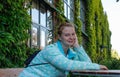 A young European woman with red hair and traces of acne on her face sits at a table in the garden. Very beautiful and fabulously c Royalty Free Stock Photo