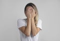 Young european woman in white t-shirt hides her face with both palms, studio photo isolated on gray background. She has social Royalty Free Stock Photo