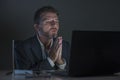 Young excited and attractive businessman in praying hands hoping to win online bet while working late night at office laptop Royalty Free Stock Photo