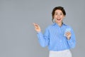 Young excited business woman using phone pointing aside isolated on grey. Royalty Free Stock Photo