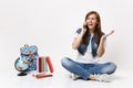 Young excited concerned woman student talking on mobile phone, spreading hands and sitting near globe, backpack, school Royalty Free Stock Photo