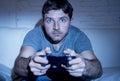 Young excited man at home sitting on living room sofa playing video games using remote control joystick Royalty Free Stock Photo