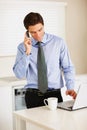 Young executive using cellphone and laptop while at the kitchen. Young business man using cellphone and laptop while at Royalty Free Stock Photo