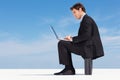 Young executive working on a laptop against clear sky. Profile view of a successful young business man working on a Royalty Free Stock Photo