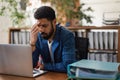 Young exhausted male employee in front of notebook in his office.