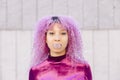Young exotic mixed race woman with afro pink hair blowing gum