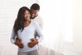 Young expectant couple staying next to window at home