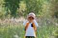 Young explorer watching with binoculars of birds in the high grass