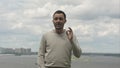 Young expressive man standing near the river, having a conversation and gesturing with his arms and hands to the camera Royalty Free Stock Photo