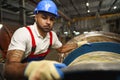 A young factory workman rolls heavy coil of electric cable