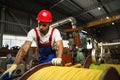 A young factory workman rolls heavy coil of electric cable