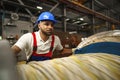 A young factory workman rolls heavy coil of electric cable