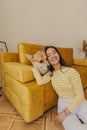 Young fair-skinned lady is having fun with corgi dog sitting on floor in cozy living room.