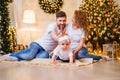 Young family with baby girl having fun time while sitting near Christmas tree. Selective focus Royalty Free Stock Photo