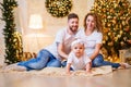 Young family with baby girl spend time together while sitting near Christmas tree. Selective focus Royalty Free Stock Photo