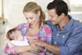 Young Family With Baby Relaxing On Sofa At Home