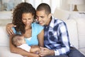 Young Family With Baby Relaxing On Sofa At Home