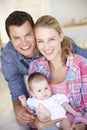 Young Family With Baby Relaxing On Sofa At Home