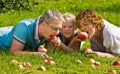 Young family bites apple, lie on a grass