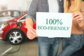 Young family buying first electric car in the showroom. Eco car. Close-up of hands holding paper with word Eco-friendly