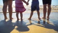 Young family with children are standing on the beach holding hands and looking at the sea