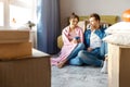 Young family couple bought or rented their first small apartment. They sit in floor and drink from blue cups. Chilling