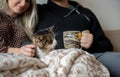 Young family couple with domestic cat and tea cup on sofa at home Royalty Free Stock Photo