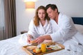 Man and woman are eating breakfast together sitting in bed in hotel room. Royalty Free Stock Photo