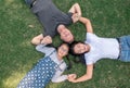 Young family with daughter laying in the park on the green grass and looking at the camera, top view. Royalty Free Stock Photo