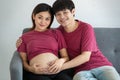 Young family husband and wife sitting on a couch. They are smiling and looking at a camera. A man and pregnant woman touching on a Royalty Free Stock Photo