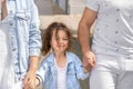 A young family leads a little curly-haired daughter by the hand along a city street