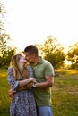 Young family mom dad walking in the evening in a Park with trees in the sunset light. Couple kissing. Happy young couple enjoying Royalty Free Stock Photo