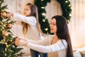 Young family mother and little daughter decorating Christmas tree at home, hanging xmas tree balls Royalty Free Stock Photo