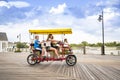 Young family riding a double surrey bicycle on a boardwalk together