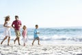 Young Family Running Along Sandy Beach On Holiday