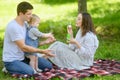 Young family sits on a blanket in park, mother blows soap bubbles, father and child catch them, play, have fun together