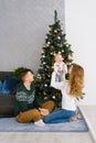 A young family sits on the floor in the living room near the Christmas tree, mom lifted up the baby in her arms, they are happy Royalty Free Stock Photo