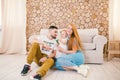 Young family sits on the floor near the couch,small daughter of a blonde one year old is learning to walk in a white dress against Royalty Free Stock Photo