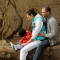 Young family sitting on a large tree and uses the tablet