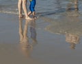 A young family with a baby is entering the warm, summer, Mediterranean Sea. Reflection on wet sand. Royalty Free Stock Photo