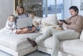 A young family with small children sit on a white sofa in a modern living room with gadgets. Love, tenderness and harmony in