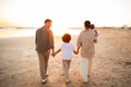 Young family taking a walk along the sea shore, holding hands with their child and walking on beach, back view Royalty Free Stock Photo