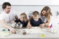 A young family with two small children in the kitchen are preparing cookie dough and laughing. The pleasure of spending time
