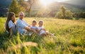 Young family with two small children sitting on meadow outdoors at sunset. Royalty Free Stock Photo