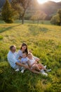 Young family with two small children sitting on meadow outdoors at sunset. Royalty Free Stock Photo