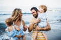 A young family with two toddler children standing on beach on summer holiday.